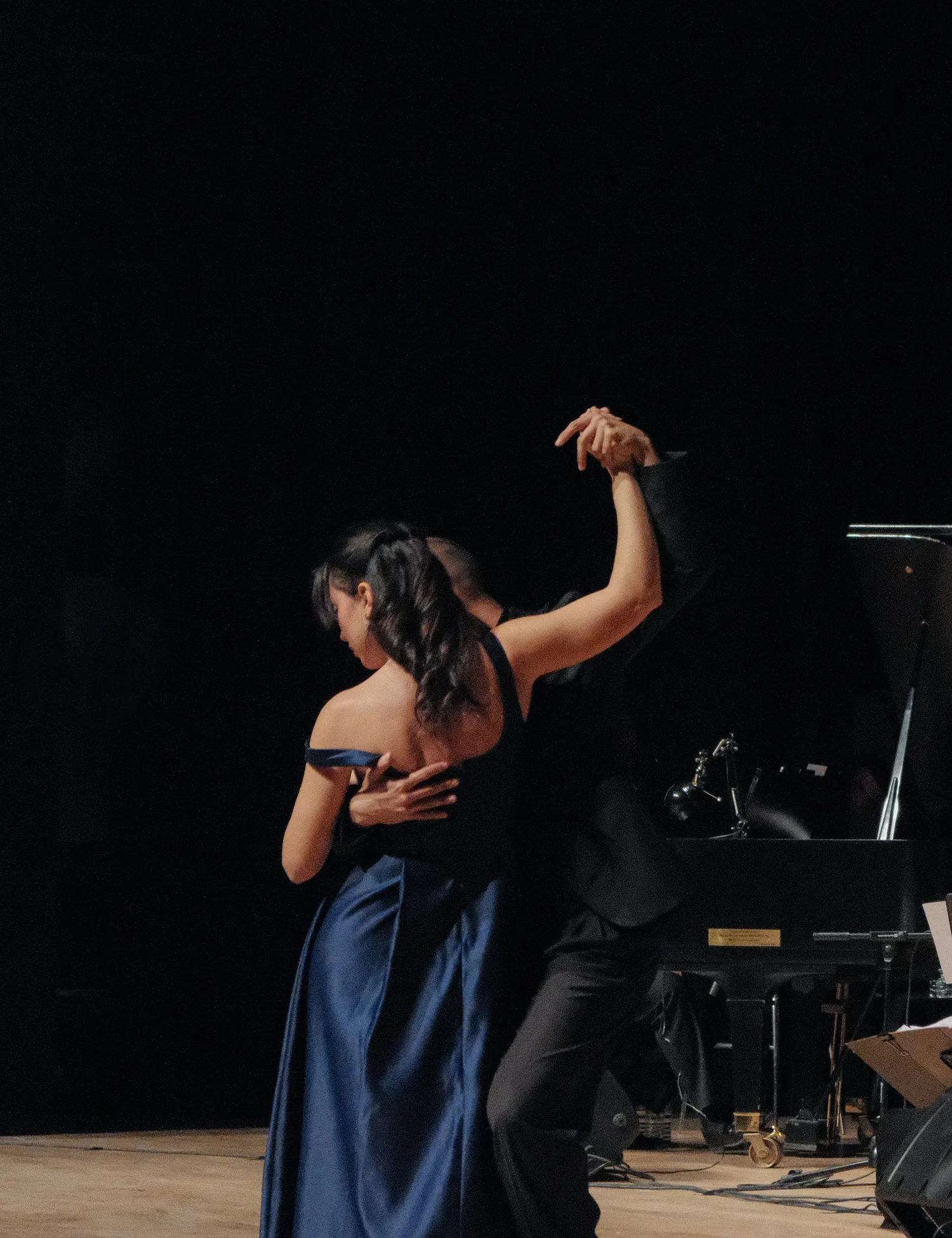 Tango dancers in a close embrace on a lit stage, representative of El Querandí's cuadro